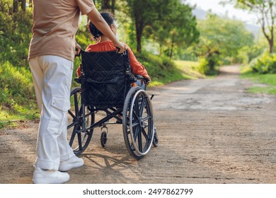 Woman sitting in wheelchair with his care helper walking on park trail  outdoor morning sunrise mountain background. Rear view - Powered by Shutterstock