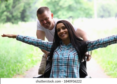 Woman is sitting in wheelchair smiling with her arms spread out man is rolling. Positive attitude towards life in people with disabilities concept