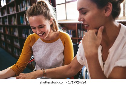 Woman sitting in a wheelchair writing in a notebook with a female teacher sitting by at school. Disabled female student studying with tutor.