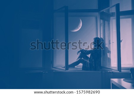 Woman sitting at the window looking at stars and the moon, Artistic Photography meditation and dreaming concept
