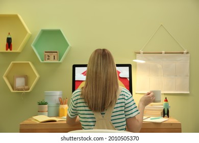 Woman Sitting At Wooden Desk With Computer Near Light Green Wall, Back View. Interior Design