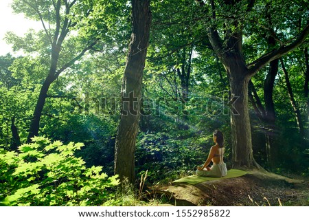 Woman sitting in yoga pose facing the sun in the forest