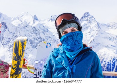 Woman with ski mask on the background of a snowboard and snow-capped mountains enjoying a sunny winter day. The concept of travel is a way of life, adventure, active recreation at a ski resort.