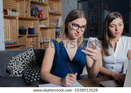 Woman skilled project manager checking e-mail on mobile phone sitting with partner in co-working space. Female smart International student reading tex message on cellphone during learning with friend [[stock_photo]] © 