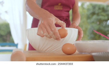 A woman is skillfully cracking eggs into a bowl that is placed on a wooden table - Powered by Shutterstock