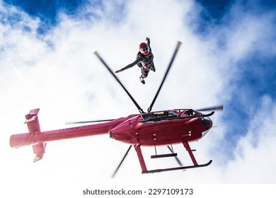 Woman skydiver leaps from bright red helicopter and blue cloudy sky