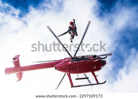 Woman skydiver leaps from bright red helicopter and blue cloudy sky