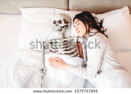 Woman sleeping in bad with funny human skeleton
