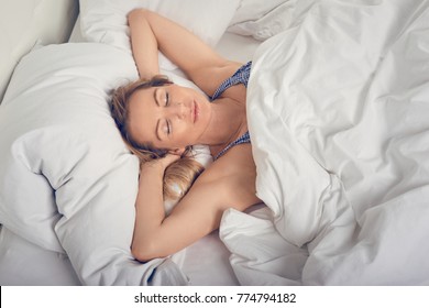 Woman sleeping in bed under white quilt with head on pillow
