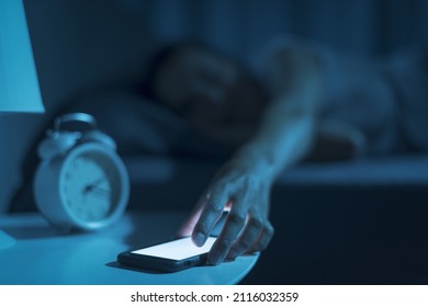 Woman sleeping in her bed and receiving a phone call late at night, she is checking her smartphone