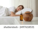 Woman sleeping at home, focus on aroma diffuser and essential oil