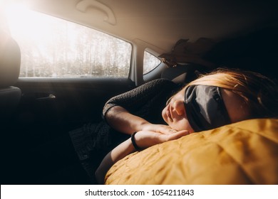 Woman is sleeping inside of car at sunset. Using sleeping mask blindfold. Automotive travel