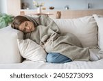 Woman sleeping on couch at home resting wrapping in plaid feeling bad symptoms. Girl suffering from seasonal flu or cold. Feel unhealthy with influenza. Tired exhausted workaholic becoming ill, sick.