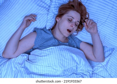 Woman Sleeping On Her Back And Snoring In Bed At Home. Night Exposure. Lady With Long Brown Hair Wearing A Nightgown. High Angle View Girl Lying In A Nightie Clean White Bed Linen With Cozy Blanket.