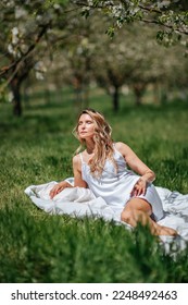 A woman sleeps on a white bed in the fresh spring grass in the garden. Dressed in a blue nightgown. - Shutterstock ID 2248492463