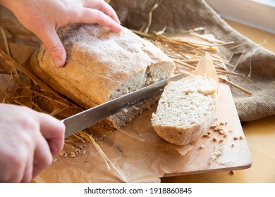 Woman slices fresh bread. hands with a knife. Freshly baked rye bread on a wooden board. Burlap, craft paper and straw on the background. Organic bread baked at home from wheat flour. Sliced bread. - Shutterstock ID 1918860845