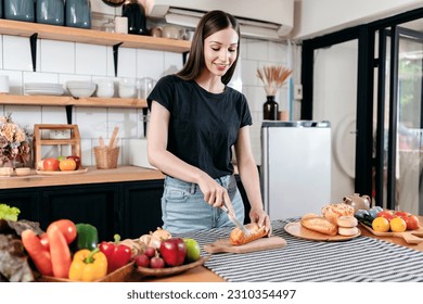 Woman slicing bread with knife on wooden cutting board and preparing fresh vegetable with fruits on the table to cooking for healthy breakfast meal in modern kitchen at home. - Powered by Shutterstock