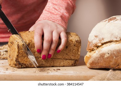 Woman slicing mixed grain bread on wooden cutting board. 