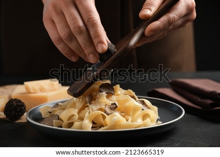 Woman slicing truffle onto tagliatelle at black table, closeup