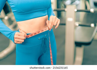 Woman with slim body measuring her waistline with tape in the fitness gym.