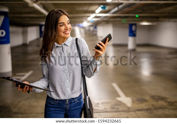 Woman with smart\
phone in underground parking lot.  Fashionable young woman texting\
on smartphone. Businesswoman in a parking garage. Woman in the\
underground car parking 