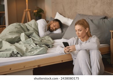 Woman with smartphone in bedroom, man sleeping in the background - Powered by Shutterstock