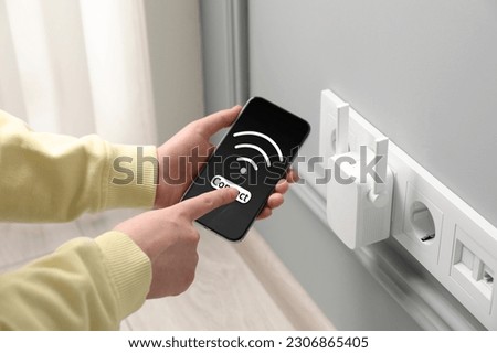 Woman with smartphone connecting to internet via wireless repeater indoors, closeup. Wi-Fi symbol on device screen