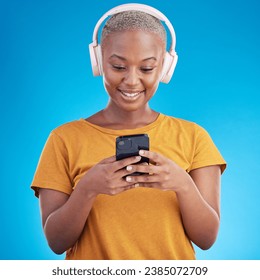 Woman, smartphone and headphones listening to music, audio streaming service or social media on blue background. Young african person or influencer chat on mobile for podcast subscription in studio - Powered by Shutterstock