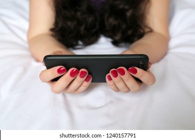 Woman with a smartphone in her hands lying on the bed. Concept of watching video, social media, online communication, home leisure, reading girl