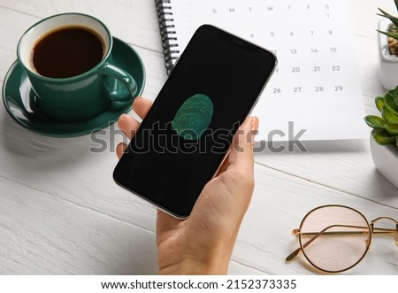 Woman with smartphone using fingerprint scanner to login into personal account at workplace
