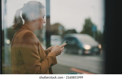 Woman with smartphone is waiting for bus at bus stop. - Shutterstock ID 2160851999