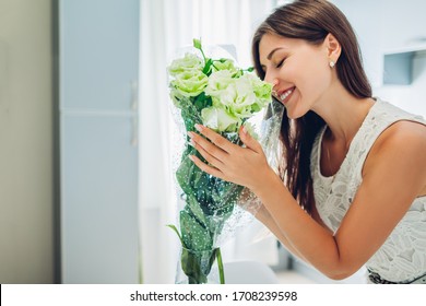Woman Smelling Bouquet Of Eustoma Flowers. Housewife Enjoying Decor And Interior Of Kitchen On Quarantine. Sweet Home