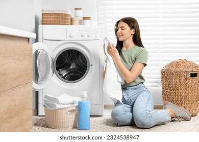 Woman smelling clean towels near washing machine in bathroom - Powered by Shutterstock