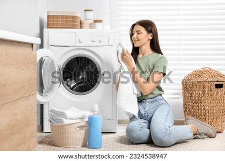 Woman smelling clean towels near washing machine in bathroom