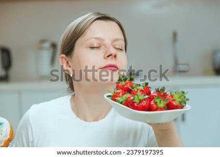 Woman smelling ripe red strawberries on white plate. Concept of eating natural sugar products and stay healthy and thin. Dieting concept, raw fruits diet