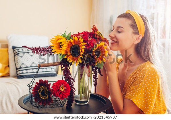 Woman smells\
bouquet of sunflowers with zinnia flowers arranging in vase at\
home. Lady enjoys fresh blooms.\
Interior