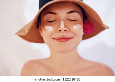 Woman Smile Applying Sun Cream  On Face. Skincare. Body Sun Protection. Sunscreen. Female In Hat Smear  Moisturizing Lotion On Skin.