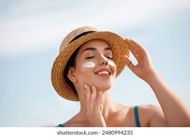 Woman smile applying sun cream on face. Skincare. Body Sun protection. sunscreen. Female in hat smear moisturizing lotion on skin. Girl holding sunscreen bottle on the beach - Powered by Shutterstock