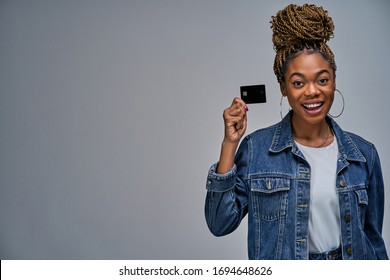 A woman with a smile in earrings holding a credit card by fingers in hands.