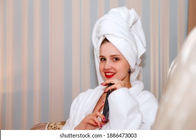 Woman Smile With Phone On Sofa Of Hotel Room After Shower. Pretty Female Of Slavic Appearance In Dressing Gown And Towel On Her Head. Happy Lady. Lesson With Smartphone. Cute Girl After Washed