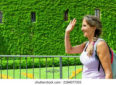 Woman Smiles As She Raises Her Arm To Greet Someone Who Is Close To Her. Athlete Happy To See Her Partner Arrive. Middle-aged Woman Reunites With An Old Friend.