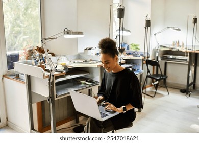 The woman smiles while typing on her laptop, surrounded by tools and elegant jewels. - Powered by Shutterstock