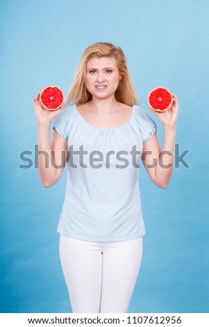 Woman smiling girl holding two halfs of red grapefruit citrus fruit in hands, on blue. Healthy diet food. Summer holidays fun concept.