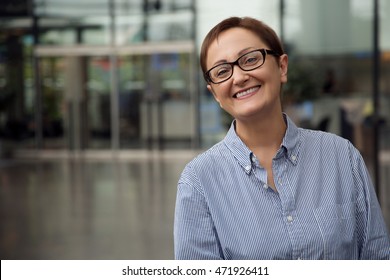 Woman smiling and looking at camera. Business woman at office. Close-up portrait of  manager, coach, lawyer, consultant, customer support, designer. Middle aged woman 40 50 years old wearing glasses