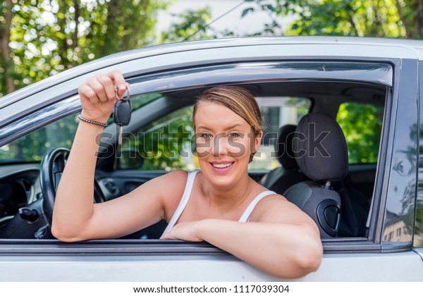 Woman smiling showing new car keys and car. Smiling\
woman sitting in car. Young woman showing key. Woman Sitting In Car\
With Key