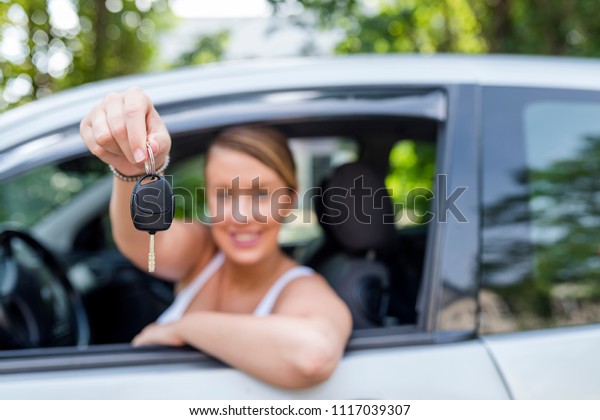 Woman smiling showing new car keys and car. Smiling\
woman sitting in car. Young woman showing key. Woman Sitting In Car\
With Key