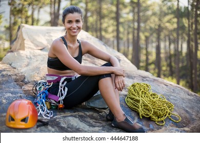 Woman smiling and sitting on a rock with climbing equipment - Powered by Shutterstock