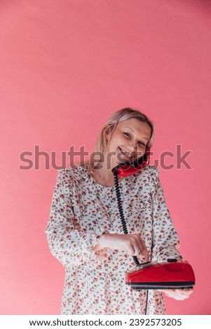 Woman smiling and talking on wired phone on pink background