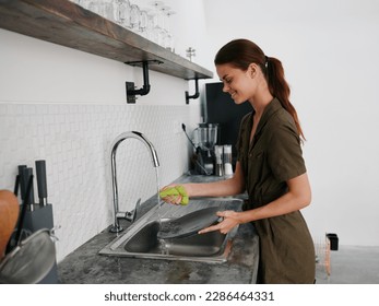 Woman smiling with teeth hands without gloves washes dishes plate with a bubble dishwashing sponge, household chores, no dishwasher, high water consumption. Stylish kitchen design, house cleaning - Powered by Shutterstock