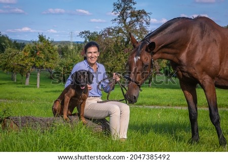 woman smiling while holding a horse and a dog sitting with her